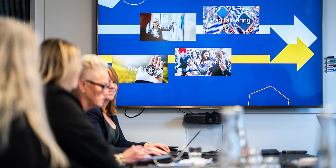 Presentations syns i bakgrunden av personer som sitter runt konferensbord