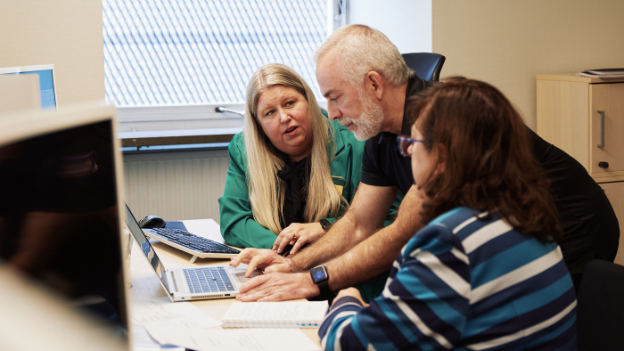 A man is leaning down and looking at a computer screen, next to him are two women. 