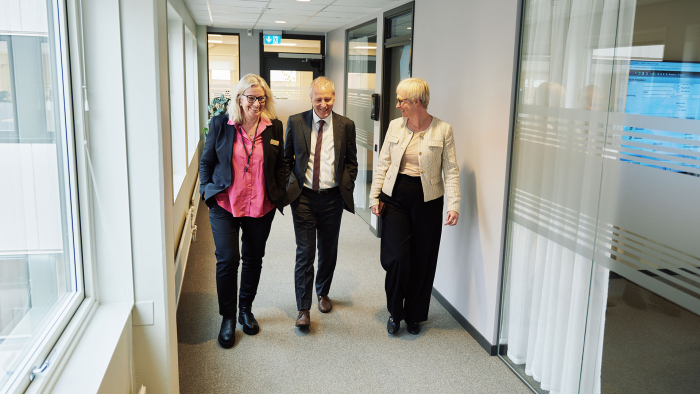 Three people walk in a row in a gray corridor.