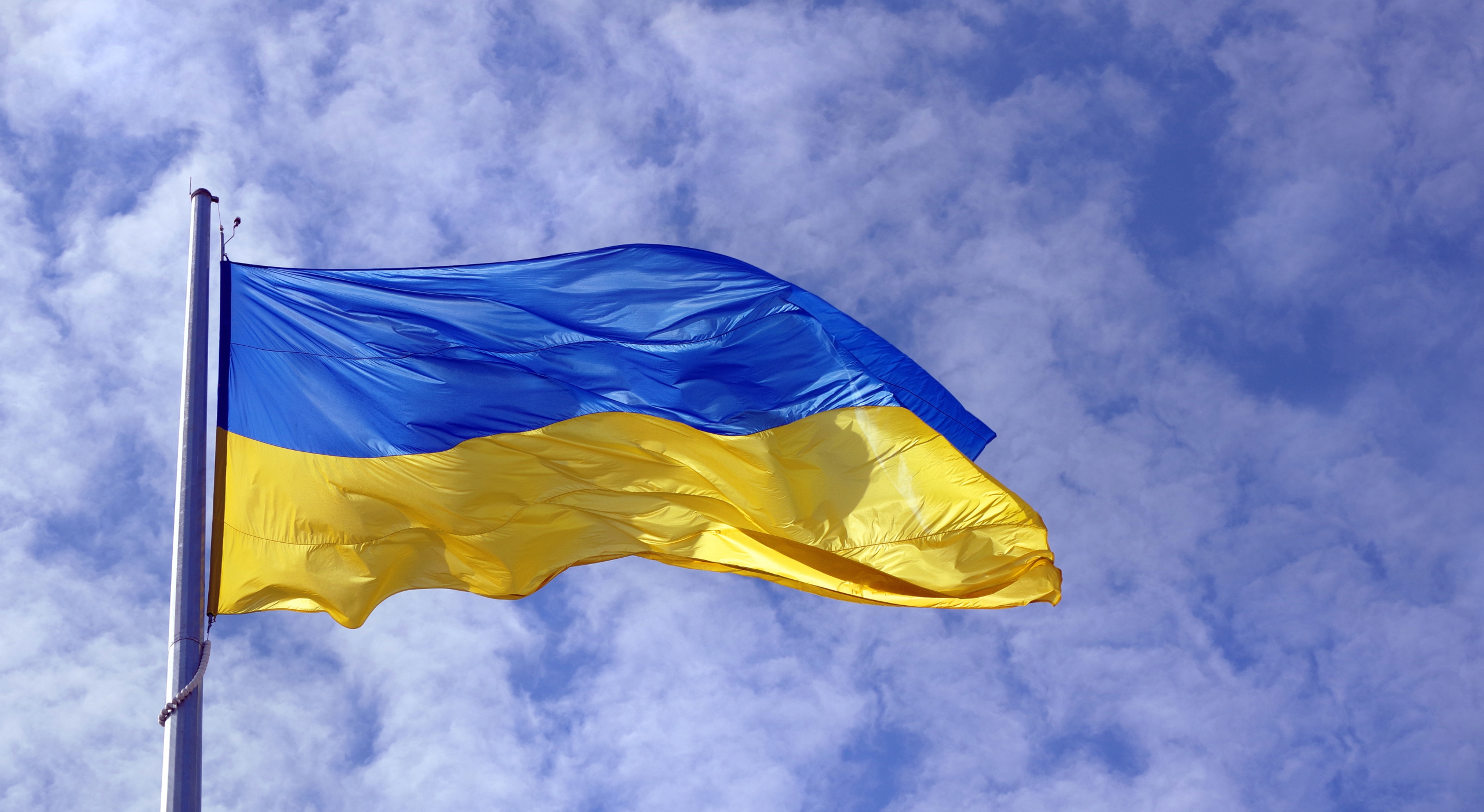 Ukrainas flagga i full vind med en halvmolnig, blå himmel i bakgrunden.